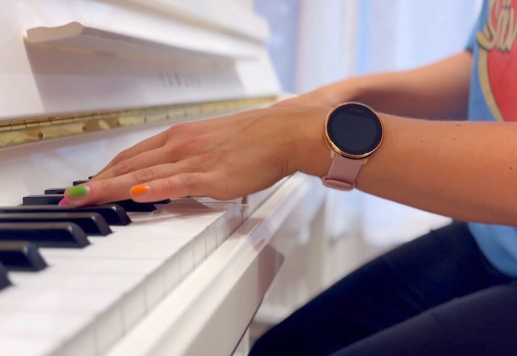 Anna - kuvituskuva 2 Kuvassa näkyvät valkoista pianoa soittavat kädet. Kynnet on lakattu monivärisesti.